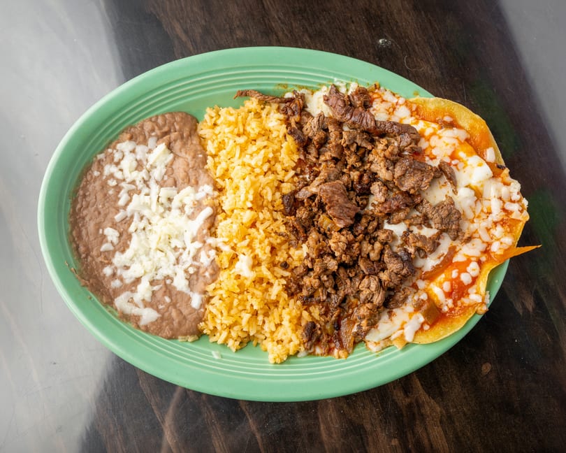 A green plate with refried beans, yellow rice, and carne asada with melted cheese.