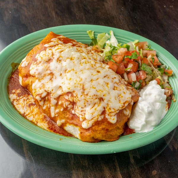 A large, cheesy burrito covered in red sauce, served with pico de gallo and sour cream.