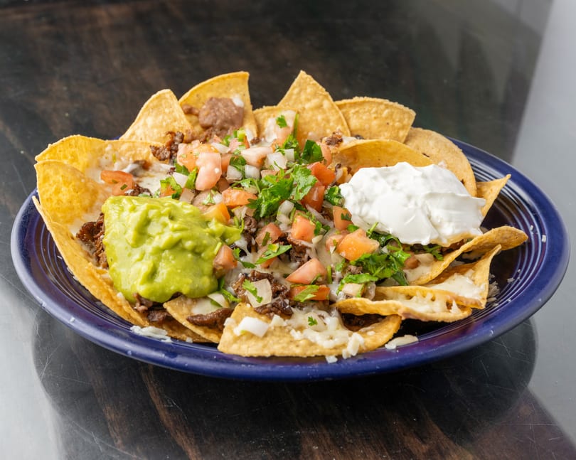 A blue plate of nachos with meat, cheese, pico de gallo, guacamole, and sour cream.