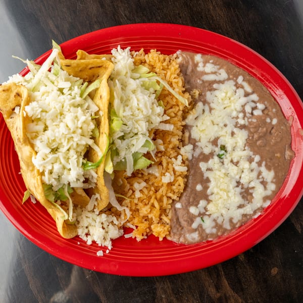 Two crispy tacos with lettuce and cheese, served with rice and refried beans on a red plate.