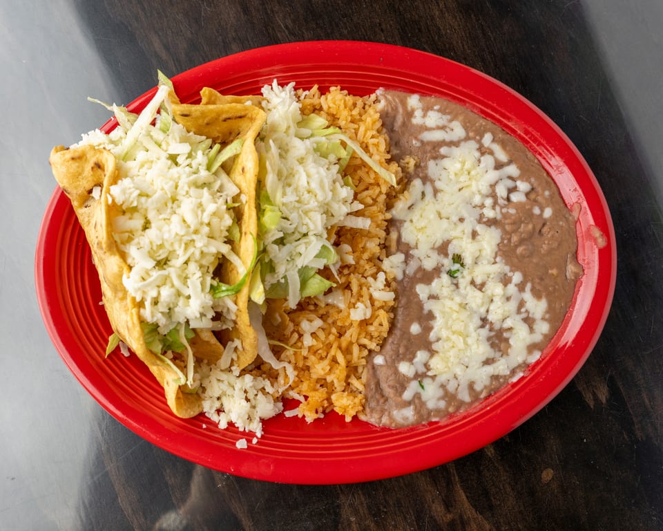 Two crispy tacos with lettuce and cheese, served with rice and refried beans on a red plate.