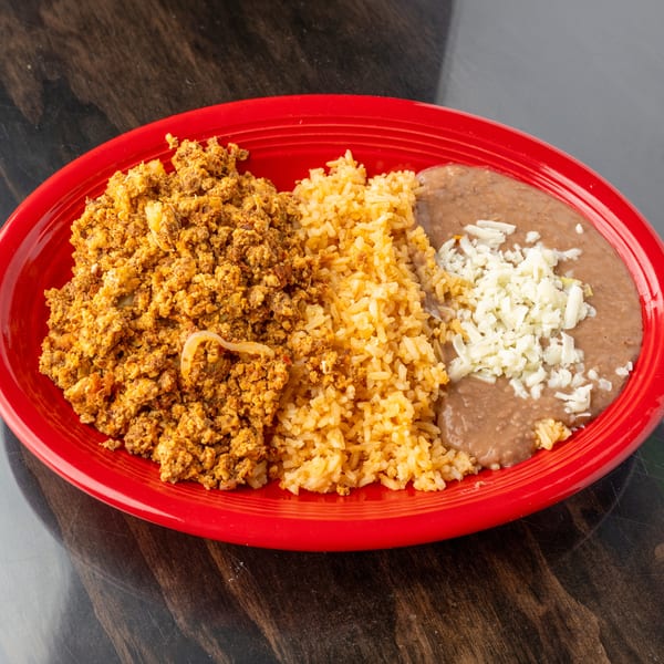 Scrambled eggs with chorizo, rice, and refried beans topped with cheese on a red plate.