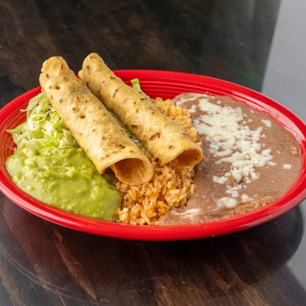 Two taquitos, rice, refried beans with cheese, guacamole, and shredded lettuce on a red plate.