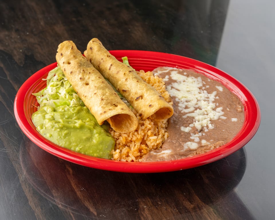 Two taquitos, rice, refried beans with cheese, guacamole, and shredded lettuce on a red plate.