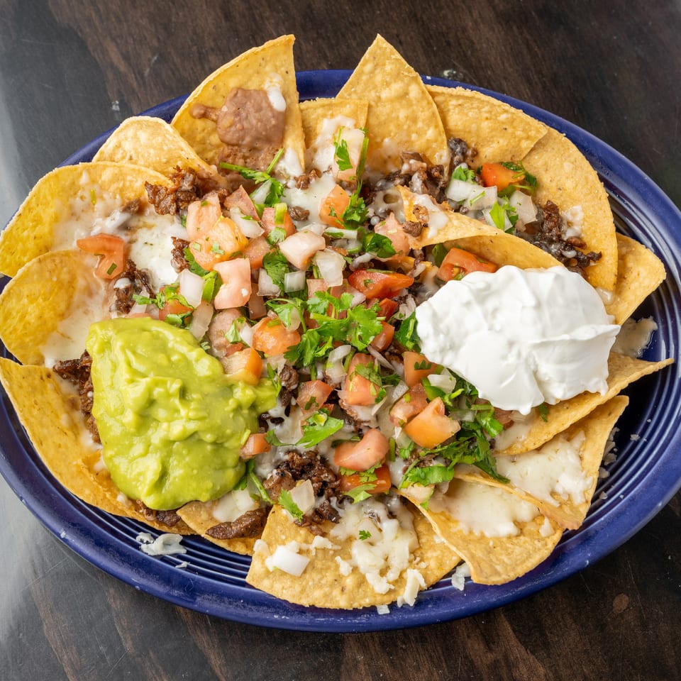 A blue plate of nachos with melted cheese, ground beef, pico de gallo, guacamole, and sour cream.