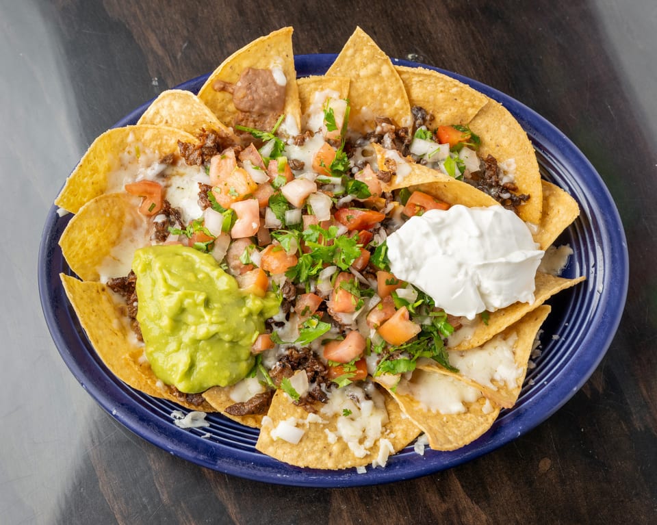 A blue plate of nachos with melted cheese, ground beef, pico de gallo, guacamole, and sour cream.