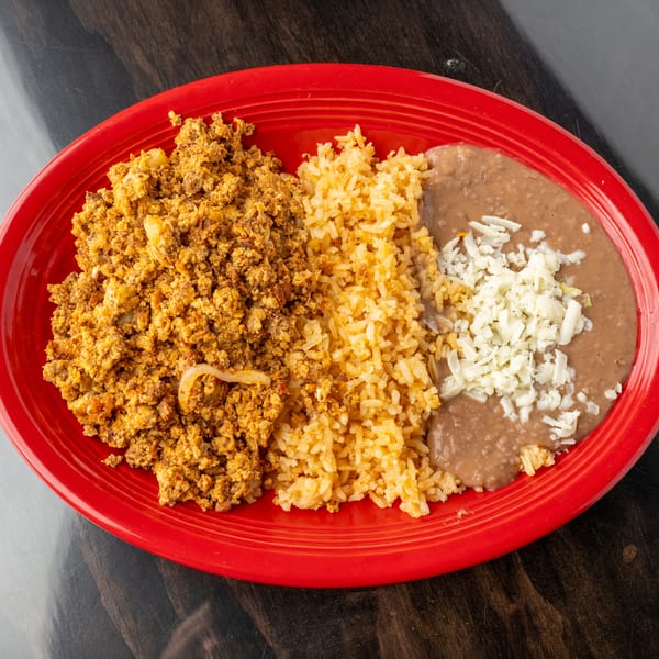 Chorizo and eggs, rice, and refried beans with shredded cheese on a red oval plate.